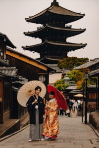 Japanese couple in traditional kimono with umbrellas at a historic pagoda in Kyoto, Japan.